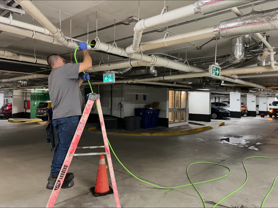 Worker using a ladder to service overhead piping in a parking garage