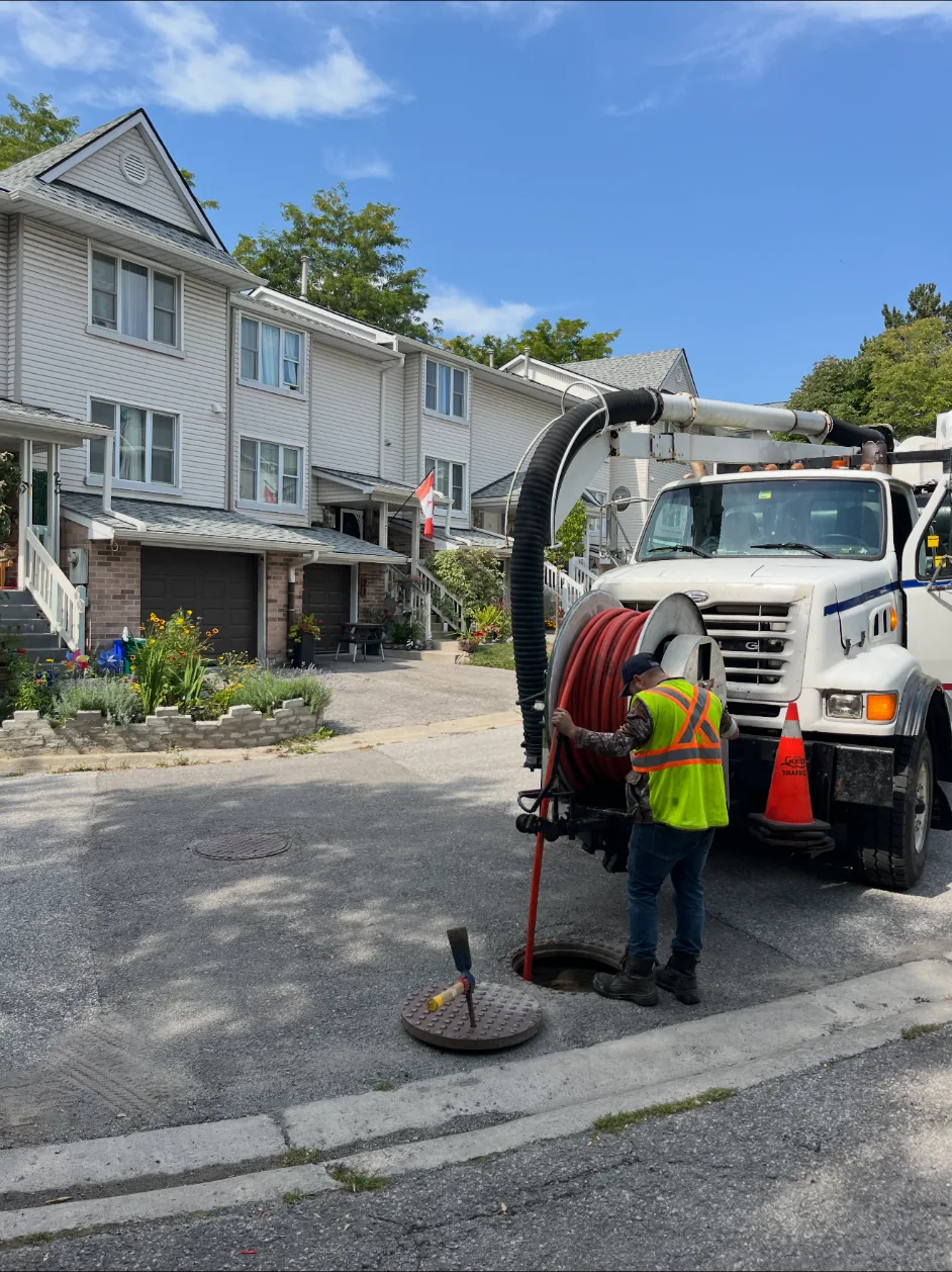 Worker operating hose equipment beside a residential manhole